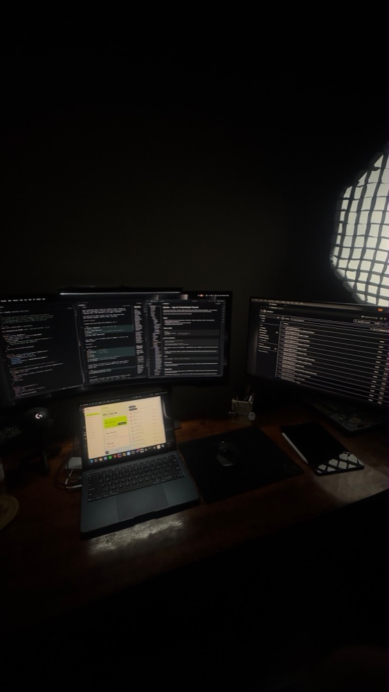 Dark home office with three monitors, laptop and softbox light